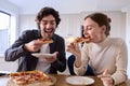 Couple In Kitchen At Home Eating Homemade Pizza Sitting At Counter