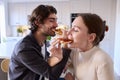 Couple In Kitchen At Home Linking Arms To Eat Homemade Pizza Sitting At Counter