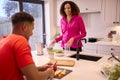 Couple In Kitchen At Home Wearing Fitness Clothing Blending Fresh Ingredients For Healthy Drink