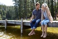 Couple, lake and sitting on jetty, outdoor and happy for hug on vacation, relax or nature in summer. Man, woman and Royalty Free Stock Photo