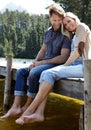 Couple, lake and sitting on pier, portrait and happy with care on vacation, relax or memory in summer. Man, woman and Royalty Free Stock Photo