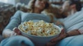 A couple leaning back on a couch passing a bowl of savory garlic herb popcorn between them as they watch a movie