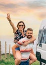 Couple looking camera having fun piggybacking next to their camper van Royalty Free Stock Photo