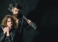 Couple in love cuddling with guitar, black background. Rock and roll concept. Guitarist with beard and girl in bra Royalty Free Stock Photo