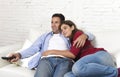 Couple in love cuddling on home couch relaxing watching movie on television with man holding remote control