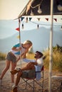 Couple in love, having small talk, young man sitting and woman standing in front of rv camper. Fun, togetherness, travel, nature