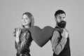 Couple in love holds big heart on pink background. Girl and bearded man with smiling faces divide toy heart