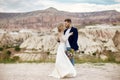 Couple in love hugs and kisses in fabulous mountains in nature. Girl in long white dress with bouquet of flowers in her hands, man Royalty Free Stock Photo