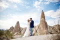 Couple in love hugs and kisses in fabulous mountains in nature. Girl in long white dress with bouquet of flowers in her hands, man Royalty Free Stock Photo