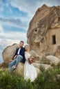 Couple in love hugs and kisses in fabulous mountains in nature. Girl in long white dress with bouquet of flowers in her hands, man Royalty Free Stock Photo