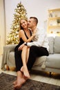 Couple in love kisses and hugs on the sofa near the Christmas tree lights. New year`s night. Christmas