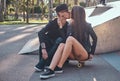 Couple in love kissing while sitting on a skateboard and in a skate park at the summertime Royalty Free Stock Photo