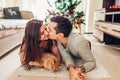 Couple in love lying by Christmas tree and playing with cat at home. Man and woman kissing Royalty Free Stock Photo