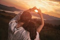 Couple in love making a heart - shape with hands, looking at the sunset