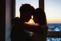 Couple in love, profile silhouettes close to each other, beautiful sunset in window at background.