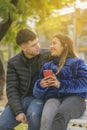Couple in love sitting on a bench in a public park with mobile phone