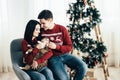 Couple in love sitting near Christmas tree and playing with cat at home Royalty Free Stock Photo
