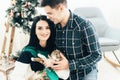 Couple in love sitting near Christmas tree and playing with cat at home Royalty Free Stock Photo