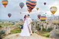 Couple in love stands on background of balloons in Cappadocia. Man and a woman on hill look at a large number of flying balloons