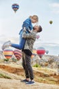 Couple in love stands on background of balloons in Cappadocia. Man and woman on hill look at a large number of flying balloons