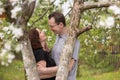 A couple in love stands at the trunk of an apple tree in a fresh spring blooming garden