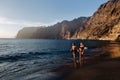 A couple in love walks on the beach against the backdrop of the Acantilados de Los Gigantes mountains at sunset