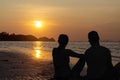 Couple in love watching the sunset together on beach travel summer holidays. People silhouette from behind sitting and enjoying Royalty Free Stock Photo