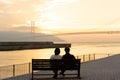 Couple in love watching sunset together on ocean travel summer holidays. People silhouette from behind sitting enjoying view. Royalty Free Stock Photo