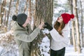 Couple in love in winter forest keeps hands in heart shape sign and send an air kiss to each other