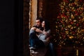 Couple of lovers hugs sitting on the windowsill in the Christmas loft studio. guy is hugging the girl.