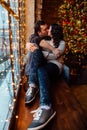 Couple of lovers hugs sitting on the windowsill in the Christmas loft studio. guy is hugging the girl.