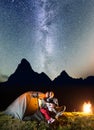 Couple lovers looking to the shines starry sky and Milky way near lighting tent in the camping at night near campfire Royalty Free Stock Photo