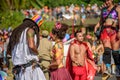 Couple of man with dreadlocks and young woman on the background of blurry man in devil costume and woman walking on stilts