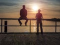 Couple man and woman looks at sunset over the sea. Man sits on a railing Royalty Free Stock Photo