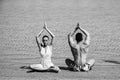 Couple meditating in yoga pose in sea, ocean water on sand at sunny summer beach in morning, idyllic vacation, relax