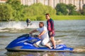 Couple of men drives Yamaha Waverunner jet ski at sunset by river bank on buildings background. Extreme sports and active summer