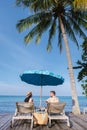 couple of men and women relaxing in beach bed looking out over the ocean under a umbrella Royalty Free Stock Photo