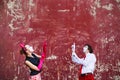 Couple mimes point to the top on a red wall.