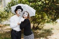 A couple of mimes walk along the pavement under umbrellas. Enamored mimes jump