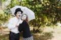 A couple of mimes walk along the pavement under umbrellas. Enamored mimes jump