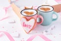 A couple of mugs with latte decorated with cinnamon hearts nearby heart shaped cookies glazed