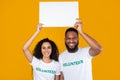 Couple Of Multiethnic Volunteers Holding White Paper Board, Yellow Background