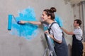 Couple in new home during repair works painting wall together. Happy family holding paint roller painting wall with blue Royalty Free Stock Photo