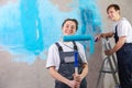Couple in new home during repair works painting wall together. Happy family holding paint roller painting wall with blue Royalty Free Stock Photo