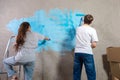 Couple in new home during repair works painting wall together. Happy family holding paint roller painting wall with blue Royalty Free Stock Photo