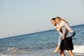 Couple, ocean waves and piggyback on vacation, smile and peace at beach or game by blue sky. People, happy and tropical Royalty Free Stock Photo