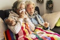 Couple of old aged senior people at home with seasonal winter cold illness disease sit down on the sof together forever - health