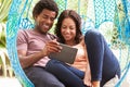 Couple On Outdoor Garden Swing Seat Using Digital Tablet