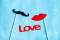 Couple paper mustache and lips props on stick and word Love on blue background.