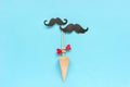 Couple paper mustache props on stick fastened clothespin heart in ice cream waffle cone on blue background. Concept Homosexuality Royalty Free Stock Photo